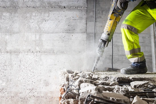 Chantier de construction en extérieur, ouvrier en vêtements haute visibilité jaune fluorescent utilisant un marteau-piqueur pneumatique pour démolir du béton armé